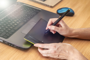 Illustrator using a graphics tablet. Woman's retoucher's hands using laptop and drawing tablet.
