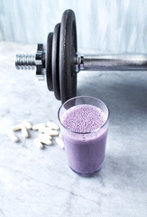 Glass of Protein Shake with milk and blueberries, Beta-alanine capsules and a dumbbell in background. Sports bodybuilding nutrition. Stone / Wooden background. Copy space.  