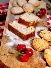 Oatmeal cookies and cherry on kitchen cutting board gingham checkered cotton fabric on table in village style for picnic. Culinary masterpiece on table. Favorite treat for tea.