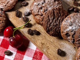 Oatmeal chocolate cookies with coffee grains and cherry, powdered sugar on kitchen cutting board with checkered fabric on wooden table in village style for picnic. Supplement for breakfast.