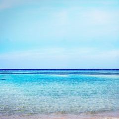 Beach on crystal with azure ocean and blue sky horizon background.