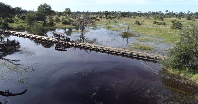 Aerial view of a safari vehicle crossing water on a pole bridge in the Okavango Delta