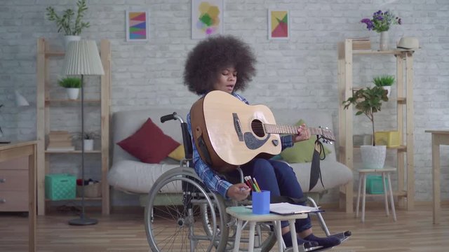 disabled african american woman with an afro hairstyle in a wheelchair plays acoustic guitar