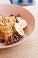 Close up of crepes with banana and chocolate sauce in a light pink bowl