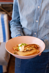 Waiter is holding a dish with folded crepes with sour cream