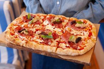 Waiter is holding roman pizza with ham and plum
