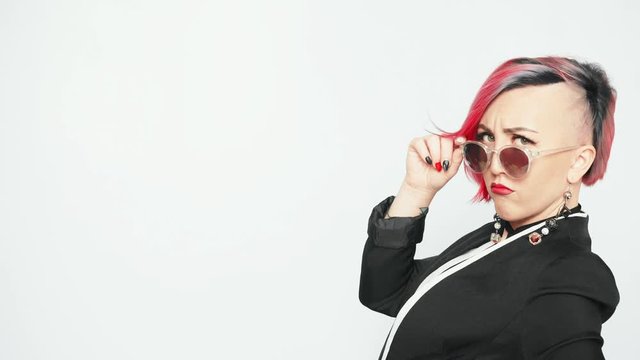 Young beautiful playful woman with pink hair looks over her sunglasses.