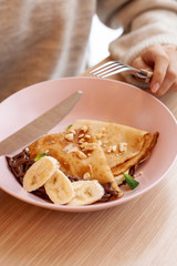 Close up of a woman having crepes with banana and chocolate sauce for breakfast