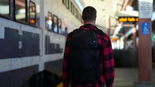 Young traveler guy walking with backpack to train at railway station in LA, California. Concept of travel active lifestyle, millennial urban life, summer vacation. 