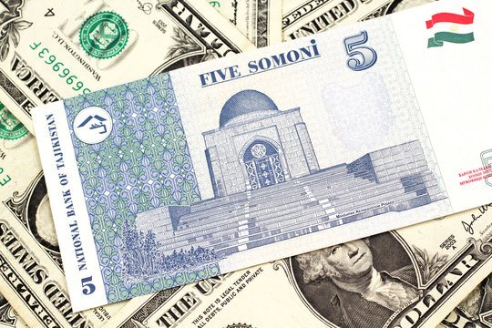 A close up image of a five somoni bank note from Tajikistan in macro with a background of American one dollar bills