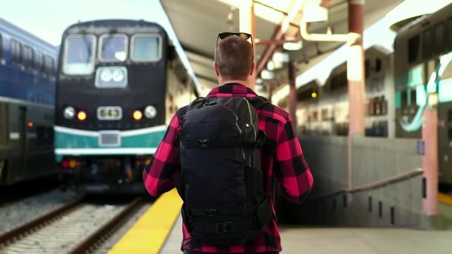 Slow motion: Millennial young male backpacker walking on platform at Los Angeles train station. Concept of summer adventure, city destination travel, millennial on road trip. 