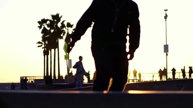 Silhouette of skater on skateboard at sunset at Venice Beach skate park, LA, California. Slow motion. Concept of modern millennial active lifestyle, friends on summer vacation sport travel.