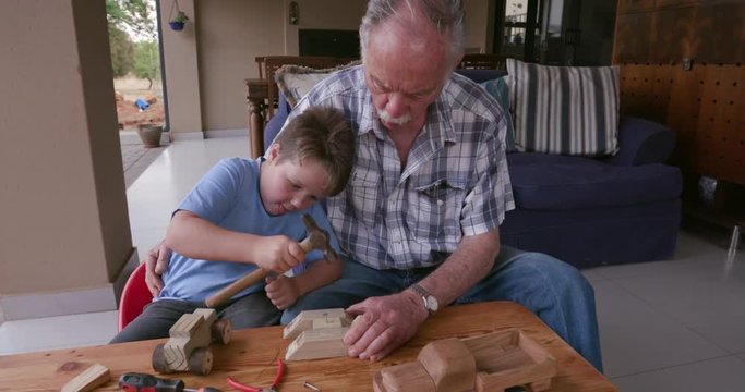 Grandfather and grandson doing some woodwork outside on a small table
