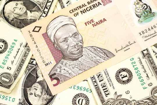A close up image of a peach colored, five Nigerian naira bank note on a background of American one dollar bills