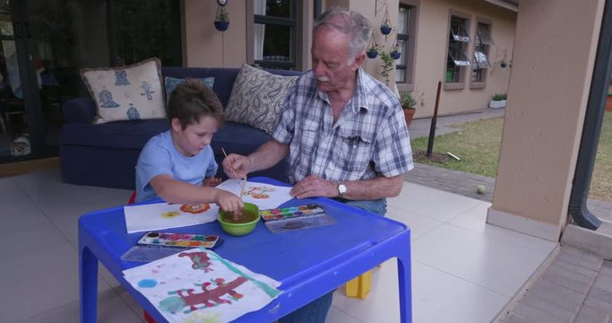Grandfather and grandson painting outside on a small table