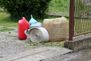 New and old plastic fuel canisters with plastic funnel next to used wide fire hose prepared for...