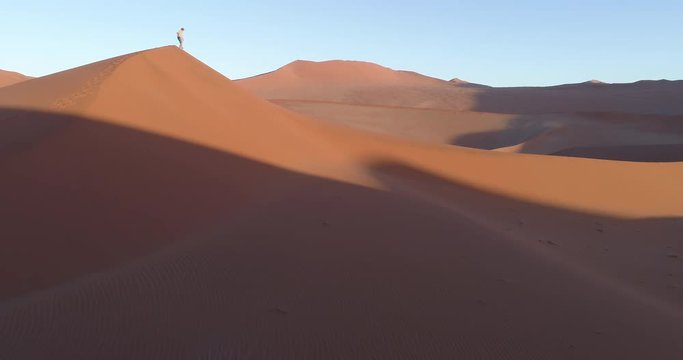 Tilt up aerial view of male tourist taking walking down one of the vast sand dunes in the Namib desert