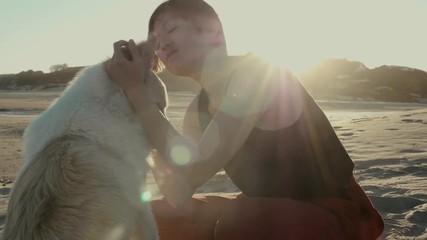 woman loving her dog on the beach at sunset with sun flare
