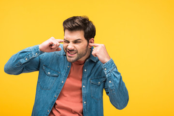 dissatisfied handsome man plugging ears with fingers Isolated On yellow