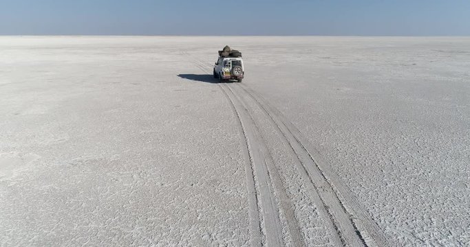 Aerial view of a 4x4 tourist safari vehicle driving across the vast Makgadikgadi Pans, Botswana 