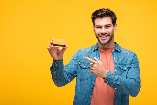 Happy Handsome Man Pointing With Finger At Credit Card Isolated On Yellow