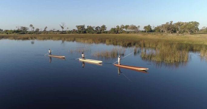 Aerial fly over view of three polers rowing their Mokoros on the waterways of the Okavango Delta