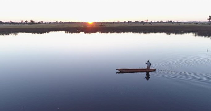 Zom out aerial view of one poler rowing a Mokoro on the waterways of the Okavango Delta at sunset