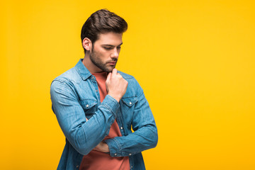 handsome pensive man touching chin Isolated On yellow with copy space