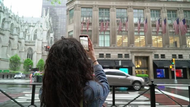 Young woman walking at Manhattan in rainy weather and taking photos