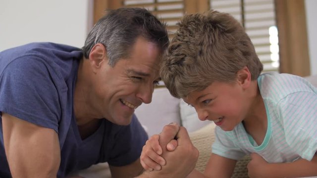 father and son arm wrestling on couch in living room 