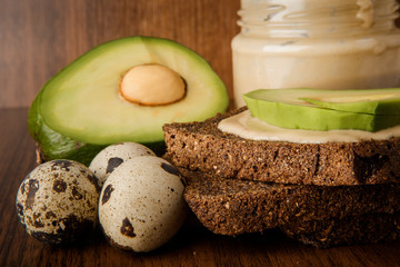 closeup jar with tahini, rye bread, sliced avocado, and quail eggs