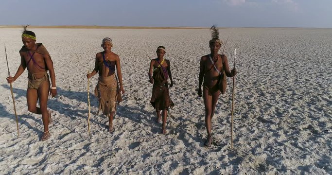 Close-up aerial view of four Bushman walking across the vast expanse of the Makgadikgadi Pans, Botswana