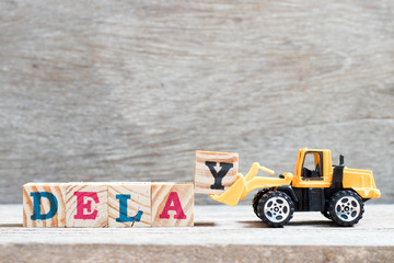 Toy bulldozer hold letter block y to complete word delay on wood background