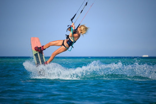 Kite surfing girl in sexy swimsuit with kite in sky on board in blue sea riding waves with water splash. Recreational activity, water sports, action, hobby and fun in summer time. Kiteboarding sport