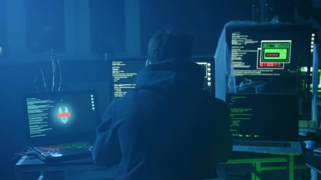 Portrait of scared and obedient computer hacker stealing important data codes on computer under the gun.