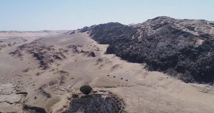 4K high aerial view with beautiful scenery of a convoy of 4x4 vehicles driving between sand dunes and mountains on the Skeleton Coast, Namib desert, Namibia