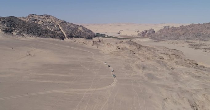 4K aerial view of a convoy of 4x4 vehicles driving between sand dunes and mountains on the Skeleton Coast, Namib desert, Namibia