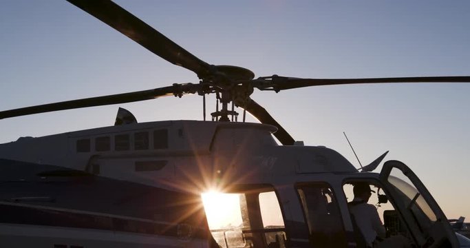 Silhouette backlit view of pilot starting up helicopter at sunrise