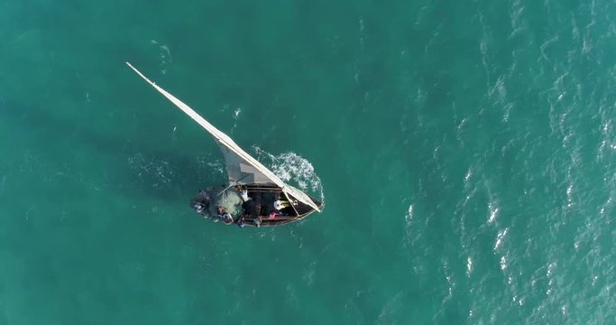 Aerial zoom out view of fisherman on a traditional dhow fishing boat heading out to sea for the days fishing