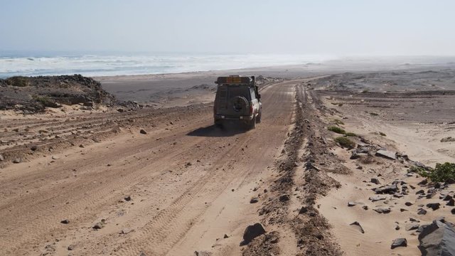 4K view of a 4x4 vehicle driving down a dirt track right next to the Skeleton coast, Namibia