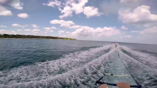 Gopro head shot on monoskier being pulled along by watersking boat. Sunny skies with blue waters. Skier crosses wake and goes round corner.