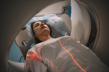 Beautiful woman lying on CT scanner bed during tomography test in hospital