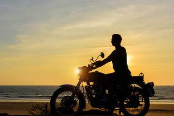Plakat Silhouette of guy on motorcycle on sunset background. Young biker are sitting on motorcycle, face in profile. Moto trip on the seaside, freedom and active lifestyle.