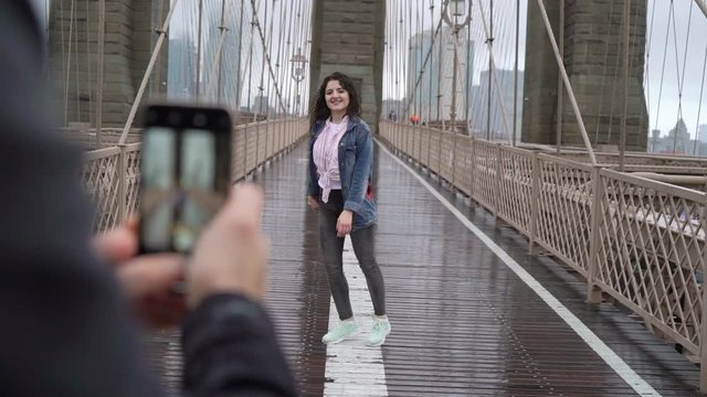Young couple walking at Brooklyn bridge in New York, man taking photo, girl posing