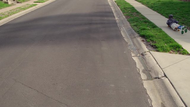 a little boy rides down the sidewalk on his belly on a skateboard
