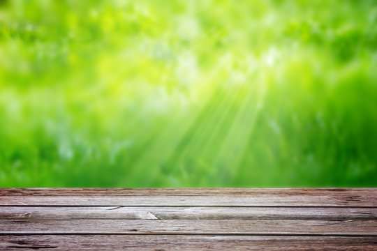 Wooden table on a background of blurred green grass with sun rays. Template, element for advertising