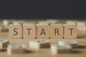 selective focus of start inscription on cubes surrounded by blocks with letters on wooden surface isolated on black