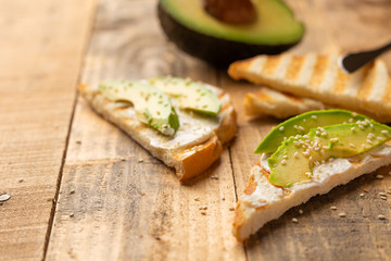 toast with philadelphia cheese, avocado pieces and sesame seeds on wooden background, healthy and healthy food , vegan food, detox