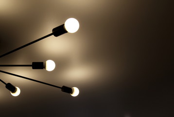 a chandelier of bright light bulbs on black beams on the ceiling and light background
