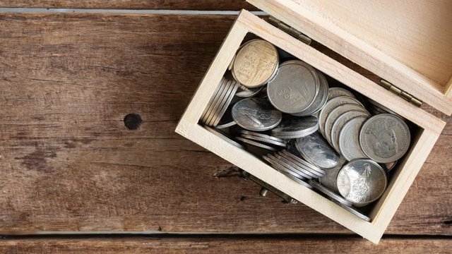 stop motion footage of silver coins Thai Baht decreasing in toy wooden chest on wood table, top view, 4K, ultra high definition resolution, thirty frame per second